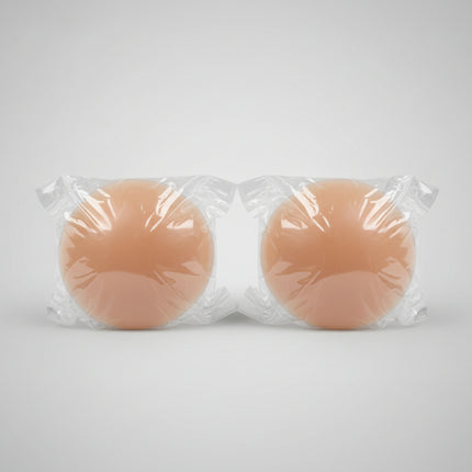 Two silicone breast forms wrapped in clear plastic on a textured surface.