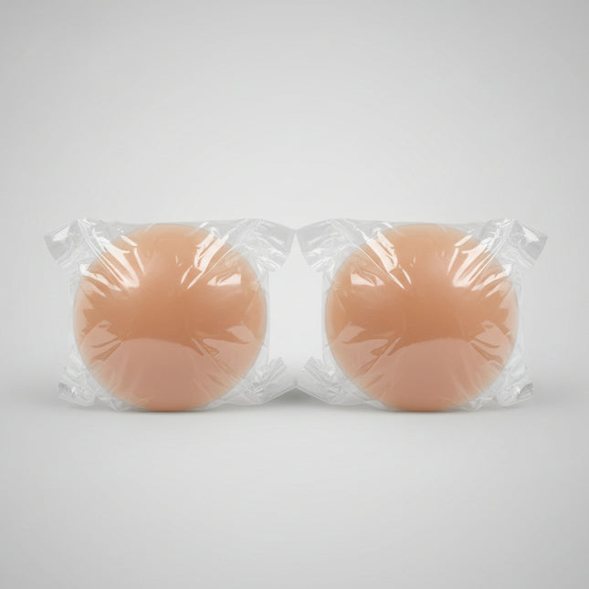 Two silicone breast forms wrapped in clear plastic on a textured surface.