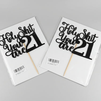 Two 'Holy Shit You Are 21' cake toppers on packaging with a neutral background.